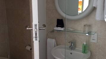 Une salle de bain avec un lavabo blanc, une cabine de douche en verre et un miroir.