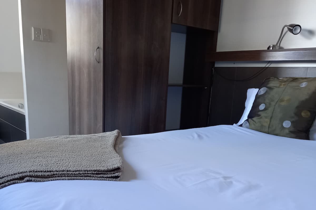 A neatly made bed with white linens, a brown throw blanket, and a pillow with circular patterns.