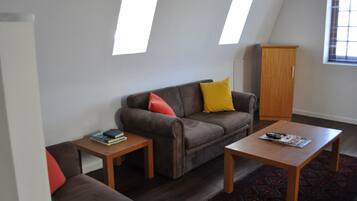 Un salon avec un canapé marron, deux tables d’appoint, un meuble en bois et un tapis à motifs.