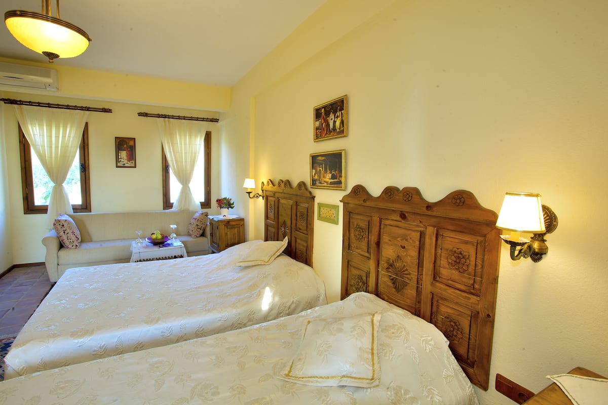 Une chambre d’hôtel avec deux lits, un canapé, une petite table avec une lampe et un luminaire fixé au mur.