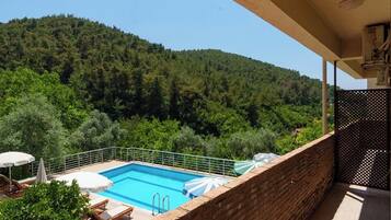 Varanda com vista para uma piscina e colinas arborizadas.