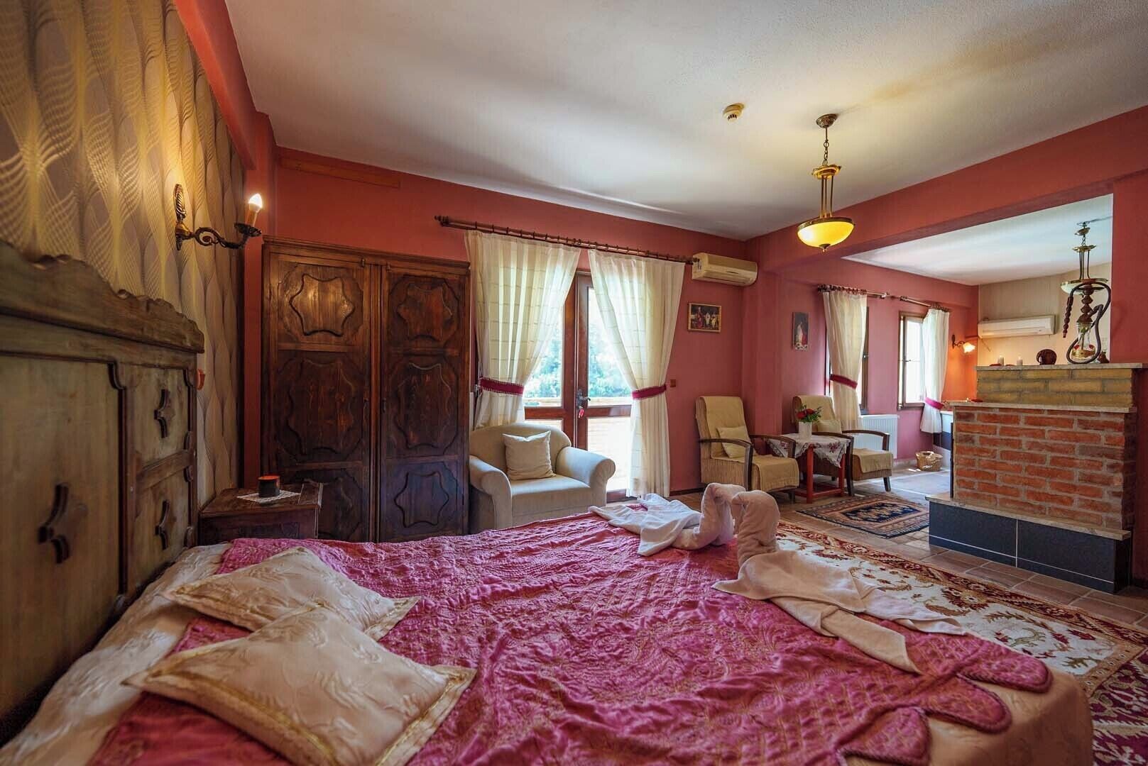 Un dormitorio acogedor con una cama grande, un armario de madera, una chimenea y una zona de estar con sillones y una mesa.