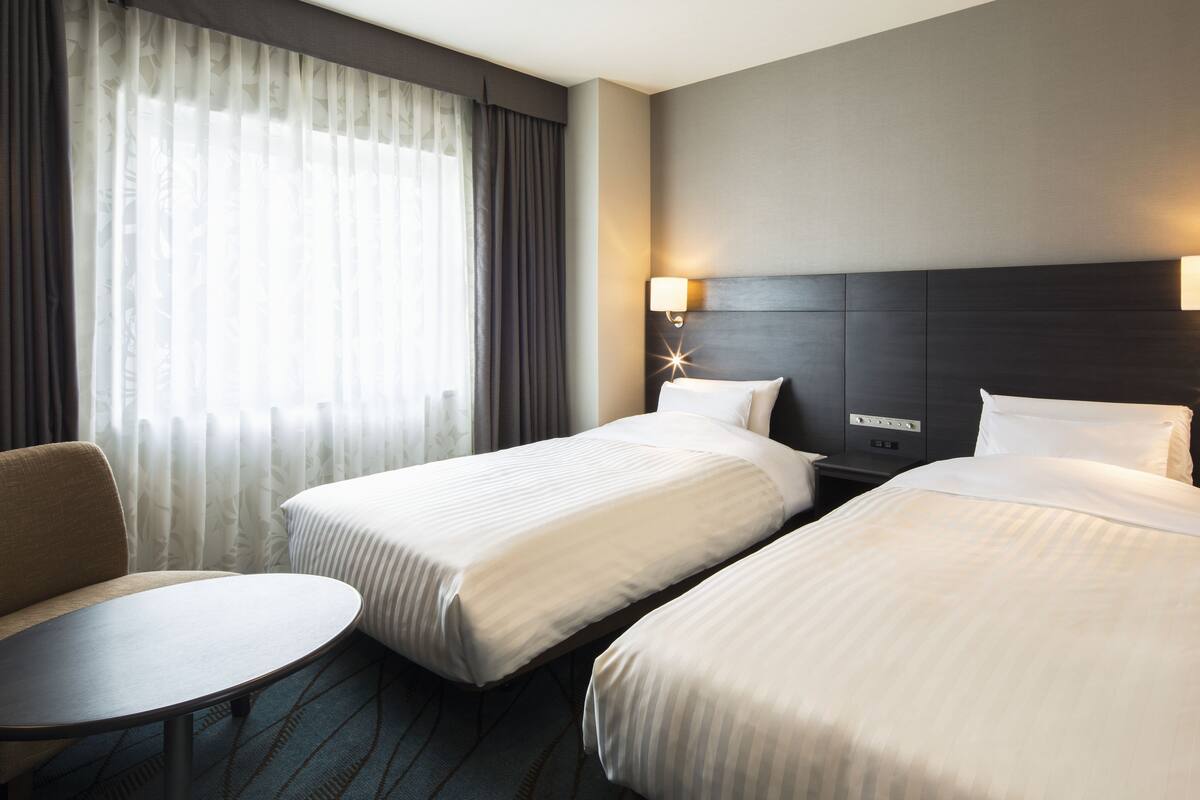 A hotel room with two beds, a small round table, and a nightstand with a lamp.