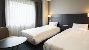 Habitación de hotel con dos camas, una mesita redonda pequeña y una mesita de noche con lámpara.