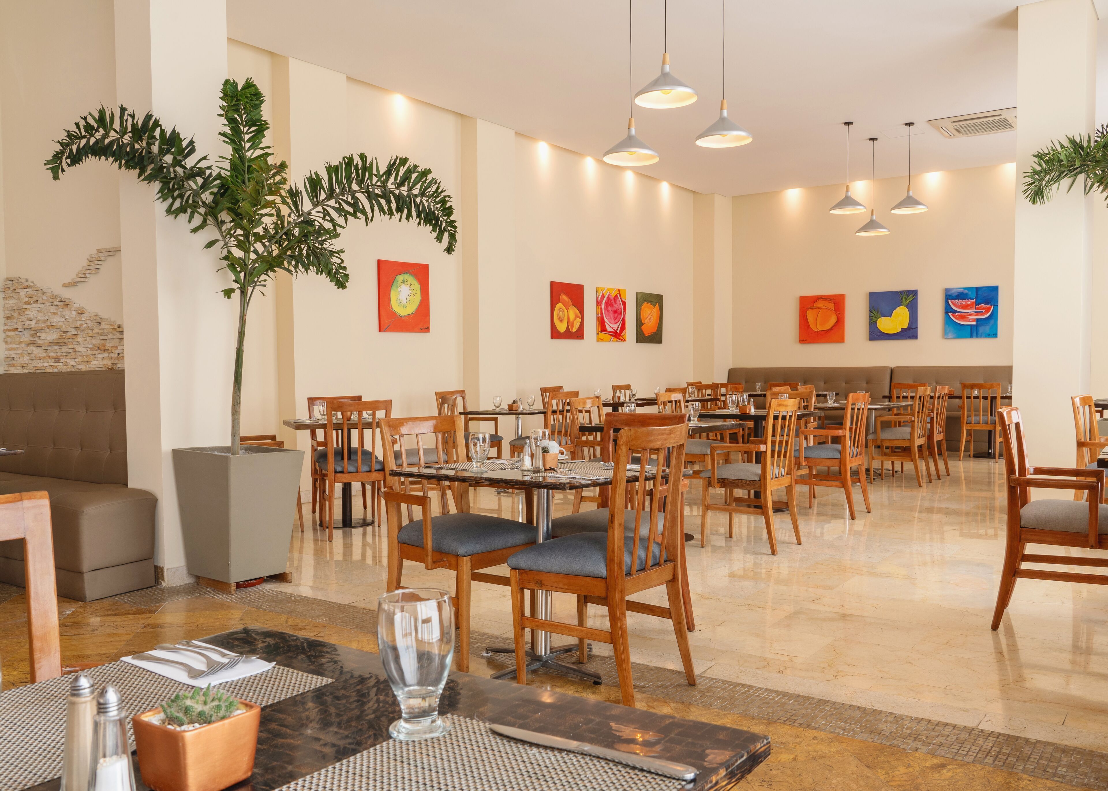 A spacious dining area with multiple tables and chairs, a large potted plant, and artwork on the walls.