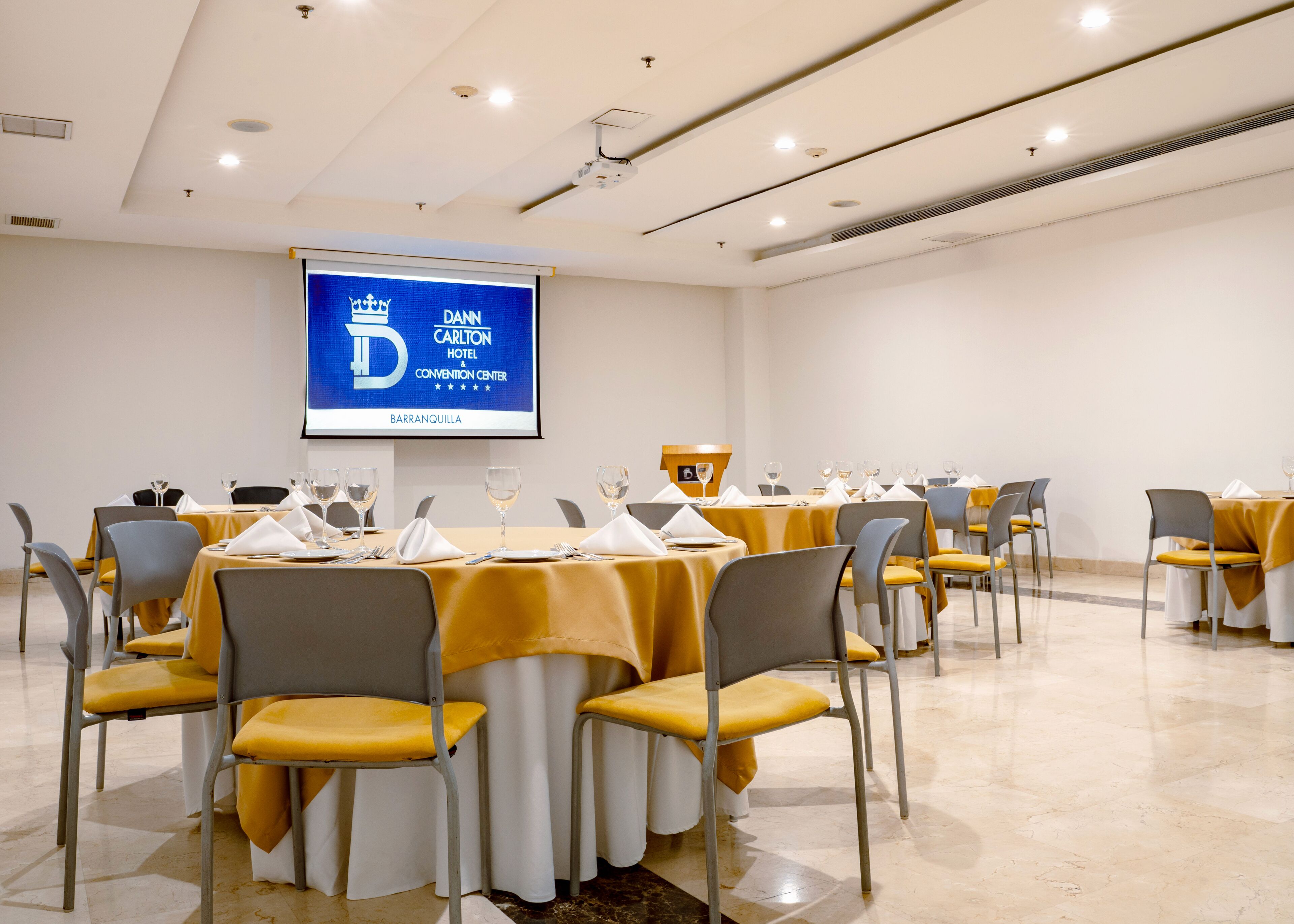 A conference room with tables set for a meeting, a screen displaying the Carlton Hotel logo, and a podium.