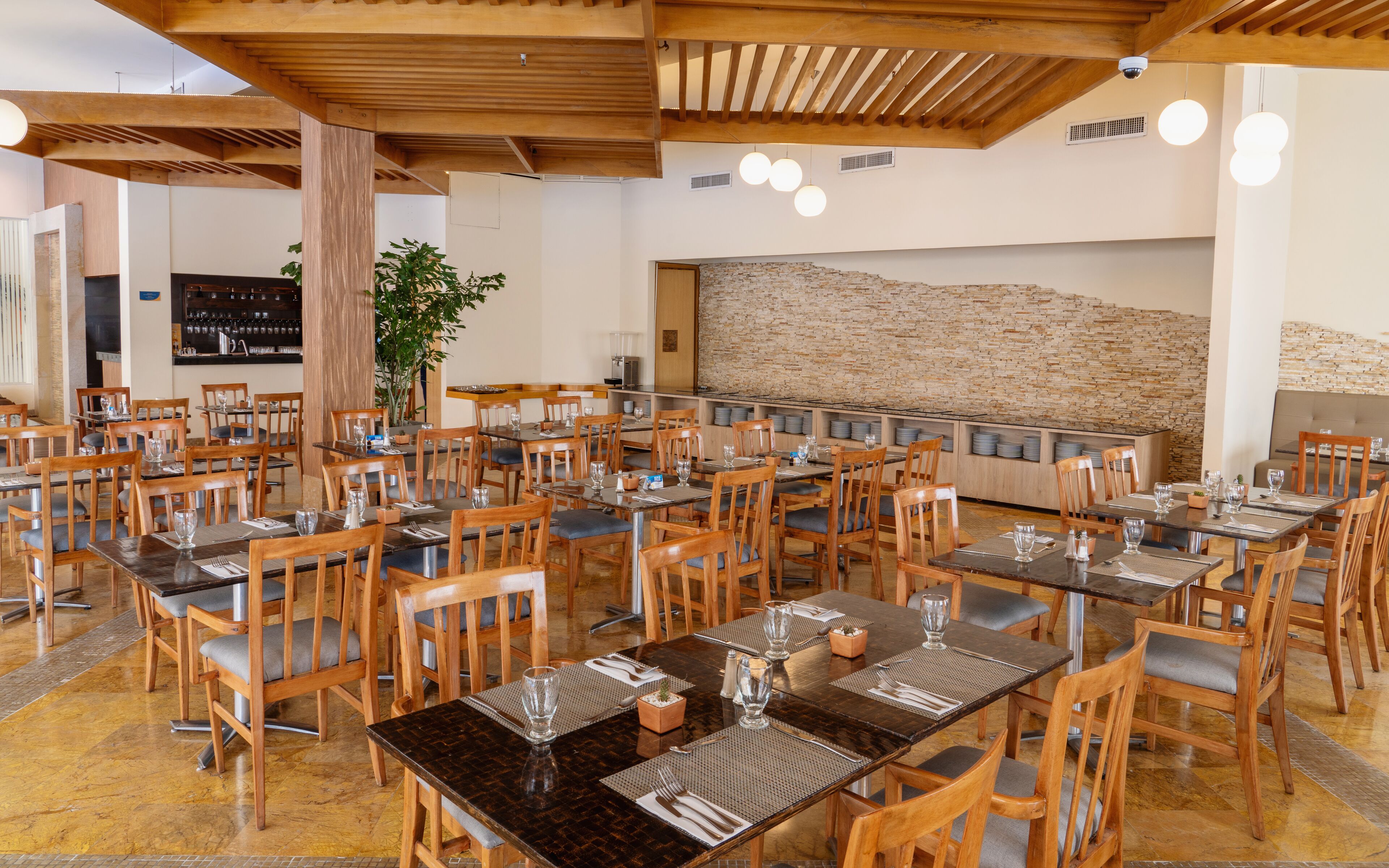 A spacious restaurant with wooden tables and chairs, a stone wall, and a bar area.