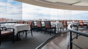 A restaurant with round tables and chairs, large windows, and a view of buildings and the sky. - Dann Carlton Barranquilla (Barranquilla)