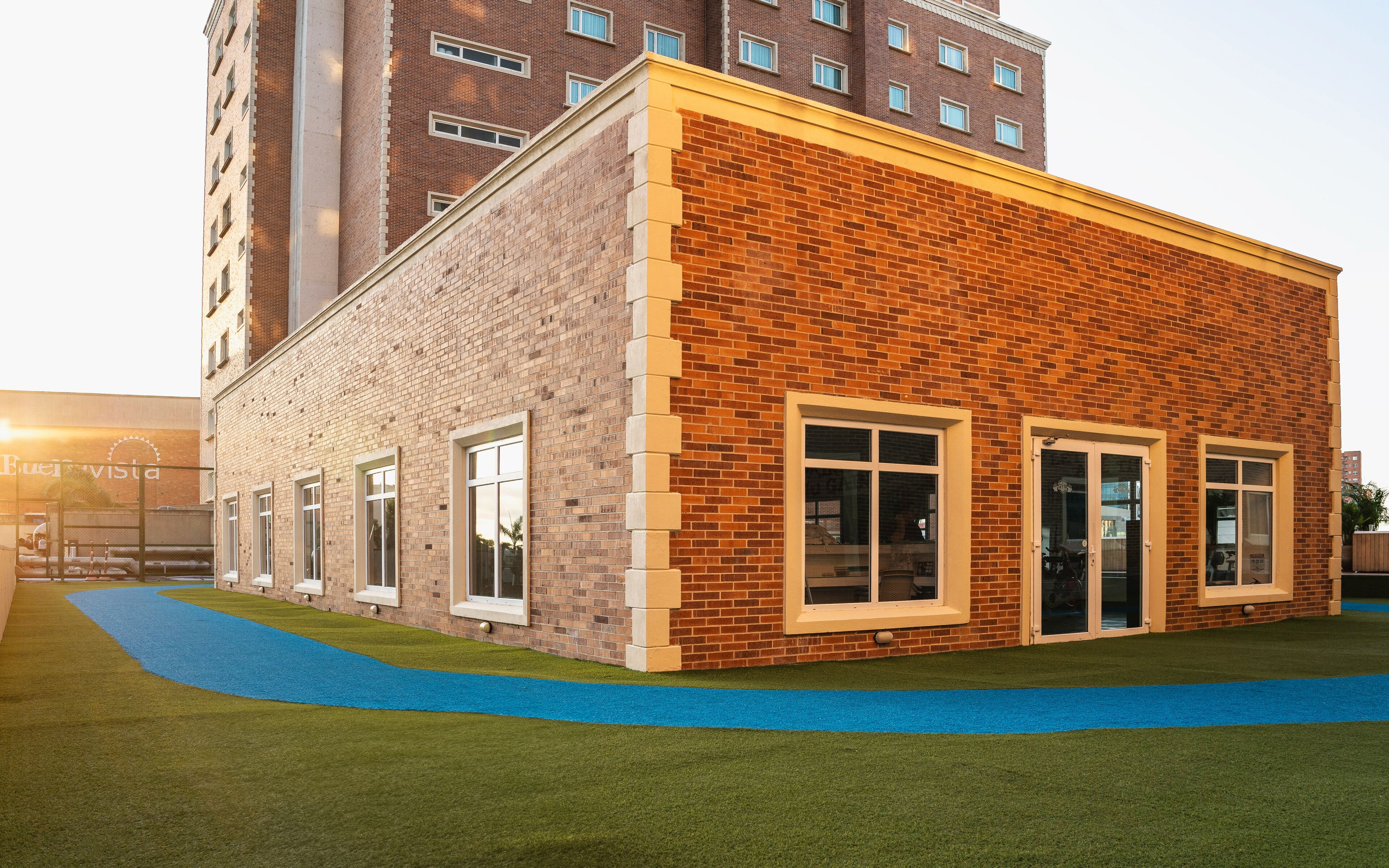 Un bâtiment moderne avec une façade en briques, de grandes fenêtres et un chemin bleu menant à l’entrée.