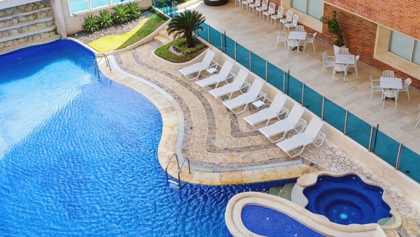 A swimming pool with a curved edge, lounge chairs, and a small hot tub. - Dann Carlton Barranquilla (Barranquilla)