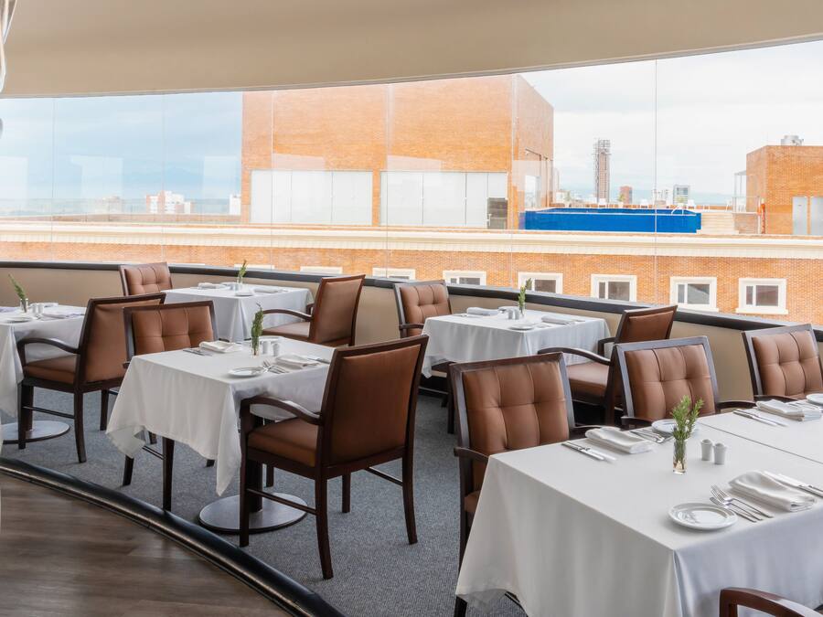 A rooftop dining area with tables set for four, overlooking a cityscape.