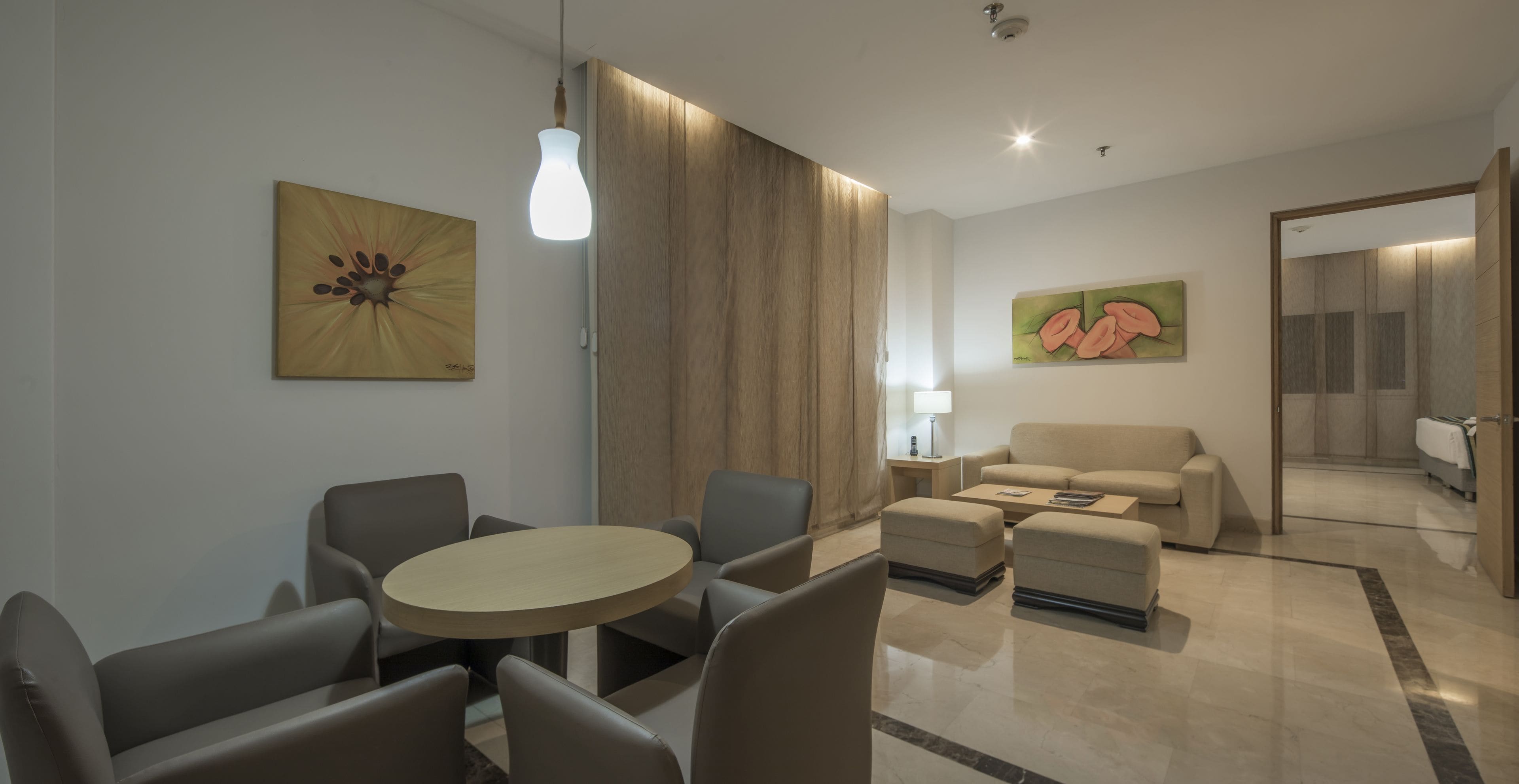 Een moderne hotelkamer met een ronde eettafel, twee banken, een bijzettafeltje en kunst aan de wanden.