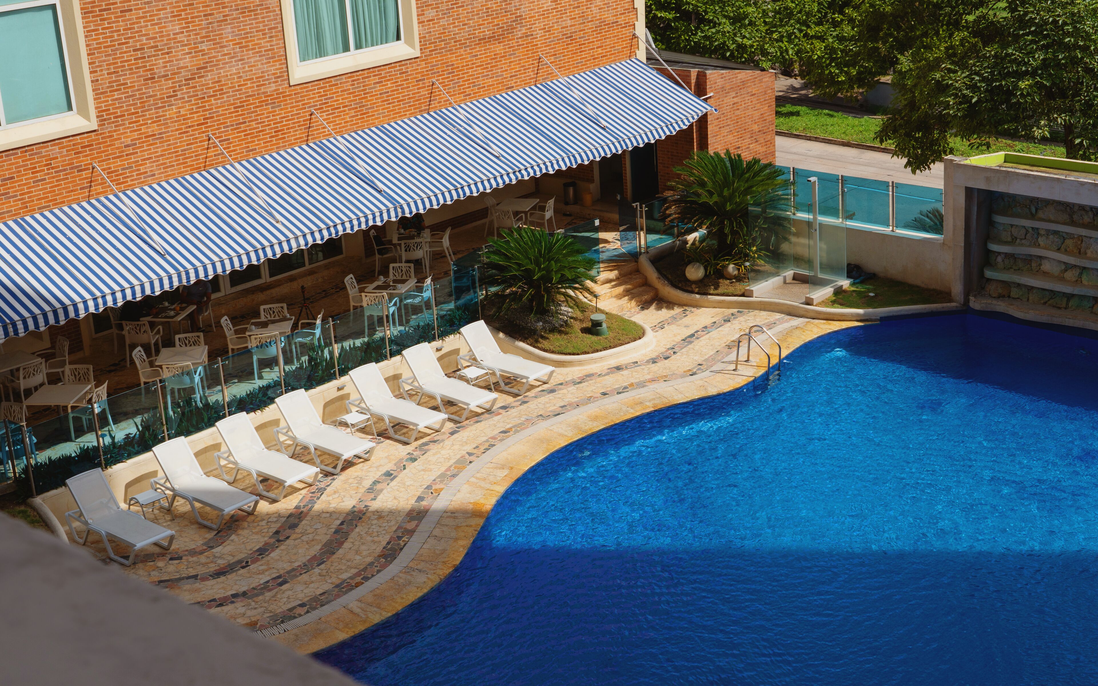Une piscine dotée d’une terrasse carrelée, de chaises longues et d’un espace salon couvert agrémenté d’auvents à rayures.