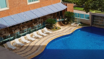 A swimming pool with a tiled deck, lounge chairs, and a covered seating area with striped awnings.