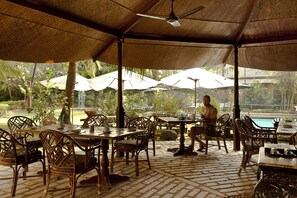 An outdoor dining area with tables and chairs, umbrellas, and a view of a pool.
