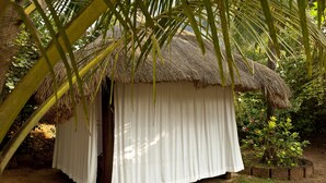 A thatched-roof hut with white curtains, surrounded by greenery. - Smith & Appy Nagoa (Calangute)