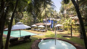 A pool area with lounge chairs and umbrellas, surrounded by palm trees and a blue building.