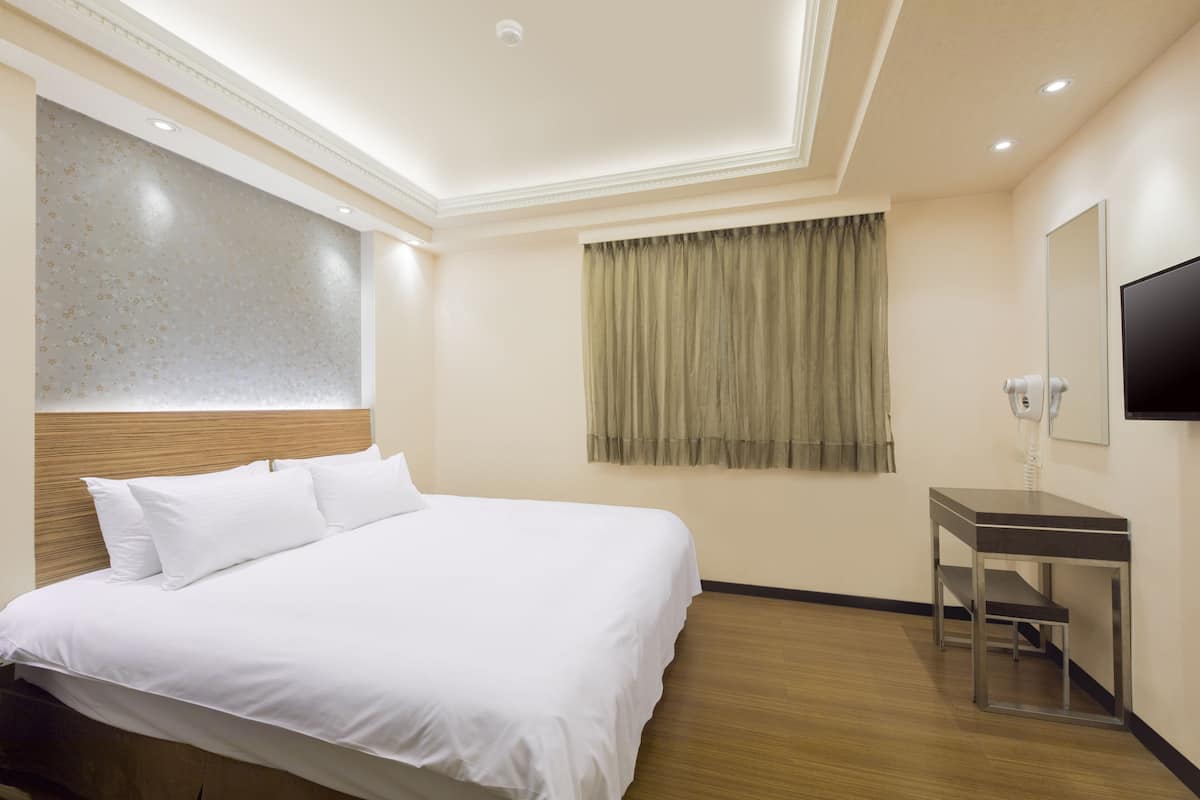 A hotel room with a large bed, a bedside table, a mirror, and a television.