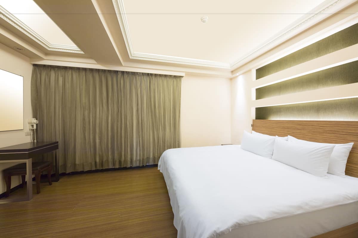 A hotel room with a large bed, a desk, and a window with curtains.