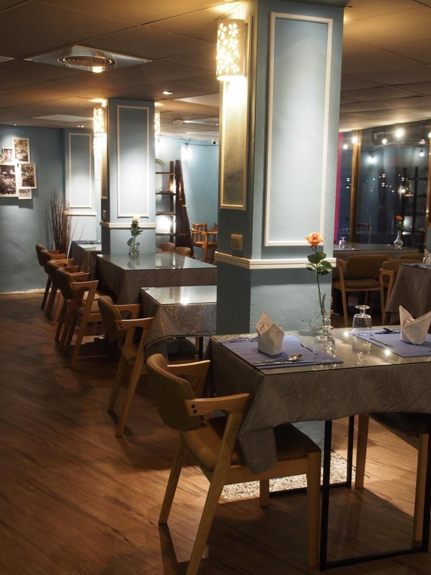 Un restaurante con una larga mesa de madera, sillas y un florero con una sola flor.