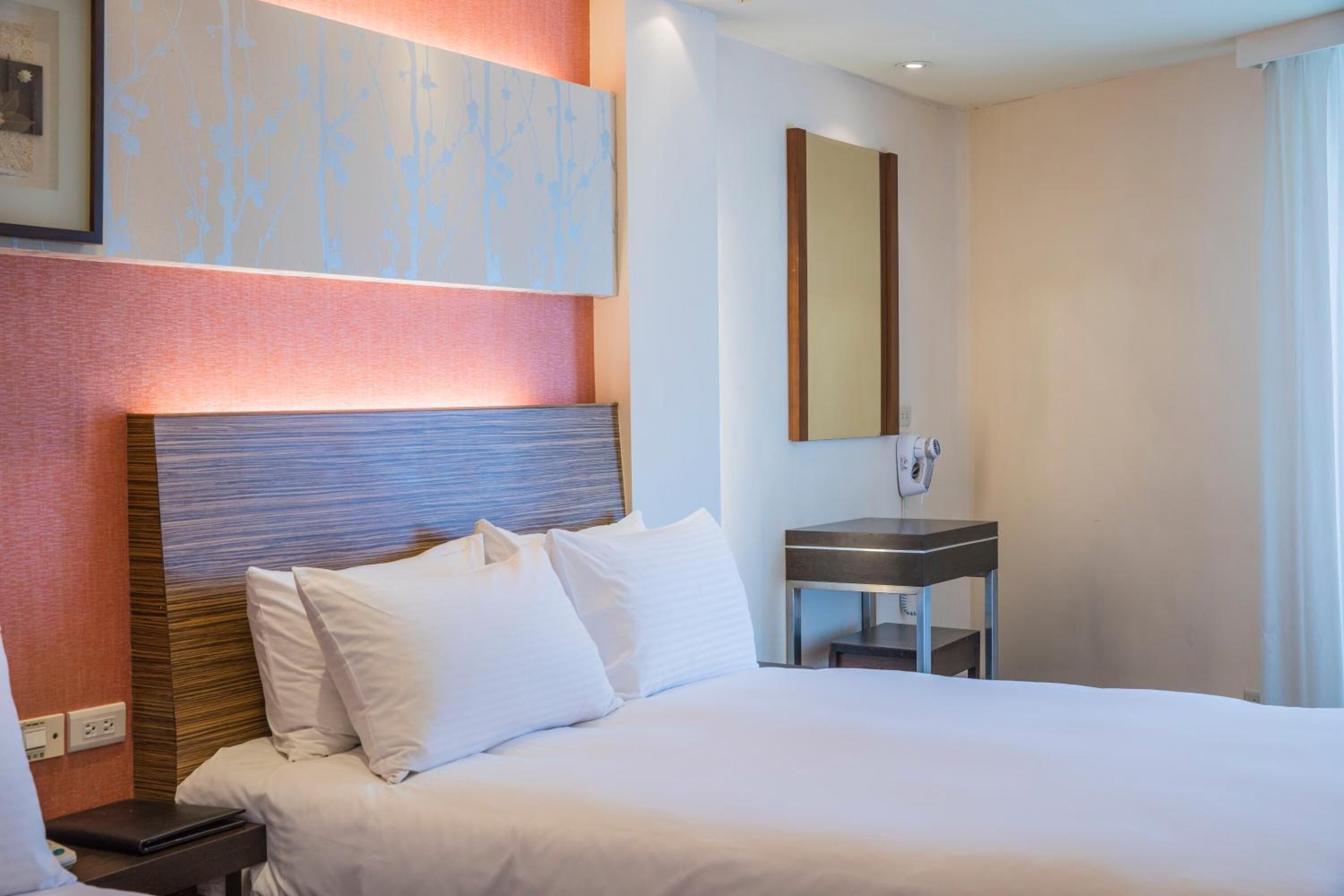 A hotel room with a large bed, a bedside table, a small desk, and a mirror on the wall.