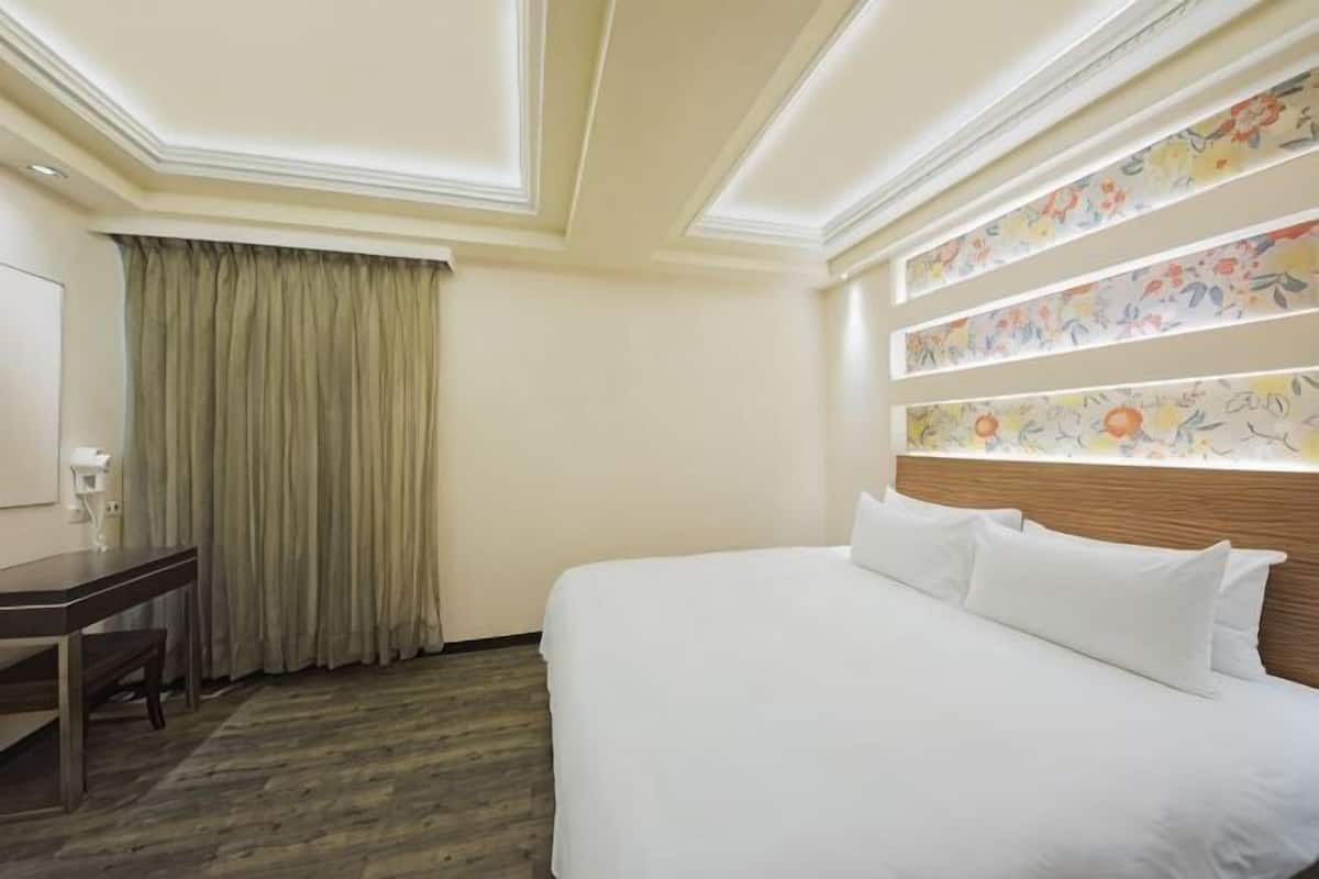 A hotel room with a bed, a desk, and a window with curtains.