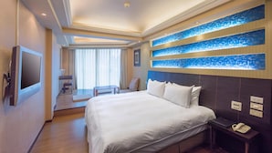 Een hotelkamer met een groot bed, een nachtkastje met een telefoon, een aan de muur bevestigde televisie, en een zithoek met een tafel en stoelen.