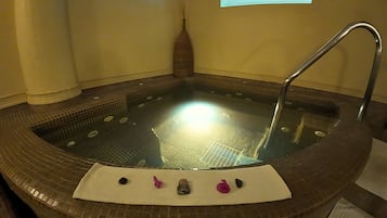 A hot tub with a tiled interior, a white mat, and a decorative vase with reeds.