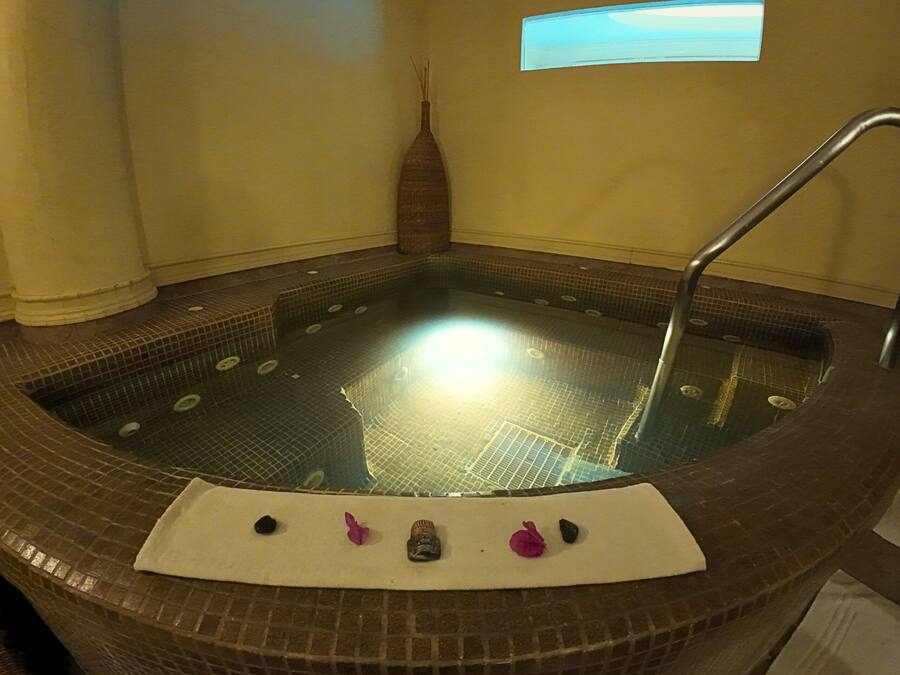 A hot tub with a tiled interior, a white mat, and a decorative vase with reeds.