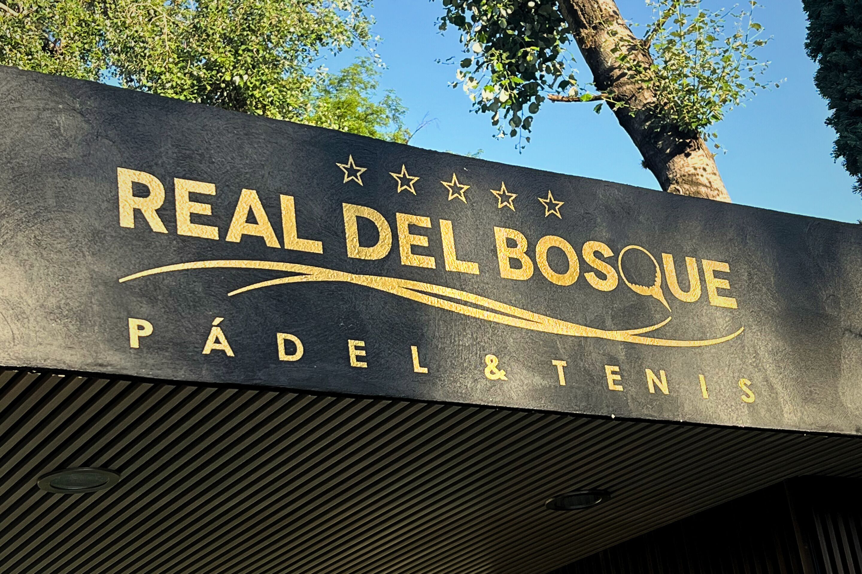 A sign for "Real Del Bosque Padel & Tenis" with a modern design and stars above the text.
