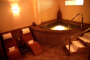 A spa area with a hot tub, two lounge chairs, and a small table with a bottle and tissue. - Hotel Real del Bosque Golf and Spa (Tula de Allende)