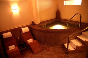 Un área de spa con un jacuzzi, dos sillones de descanso y una mesita con una botella y pañuelos.