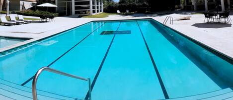 Piscina rectangular con escalera de metal, rodeada de sillones de descanso y sombrillas.