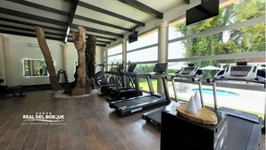 A gym with treadmills, stationary bikes, and a pool visible through large windows. - Hotel Real del Bosque Golf and Spa (Tula de Allende)