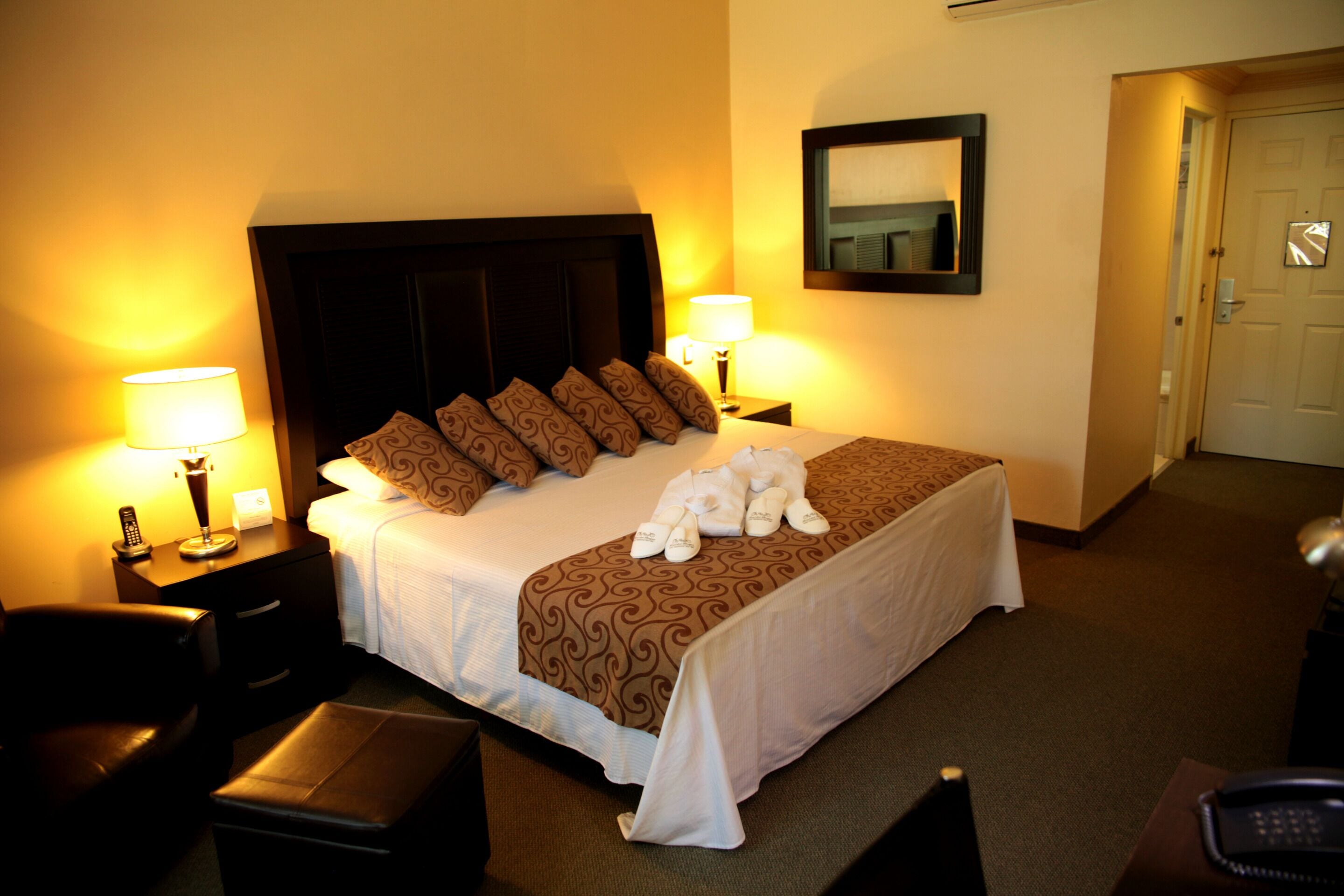 A hotel room with a large bed, two bedside tables with lamps, a chair, and a desk with a telephone.