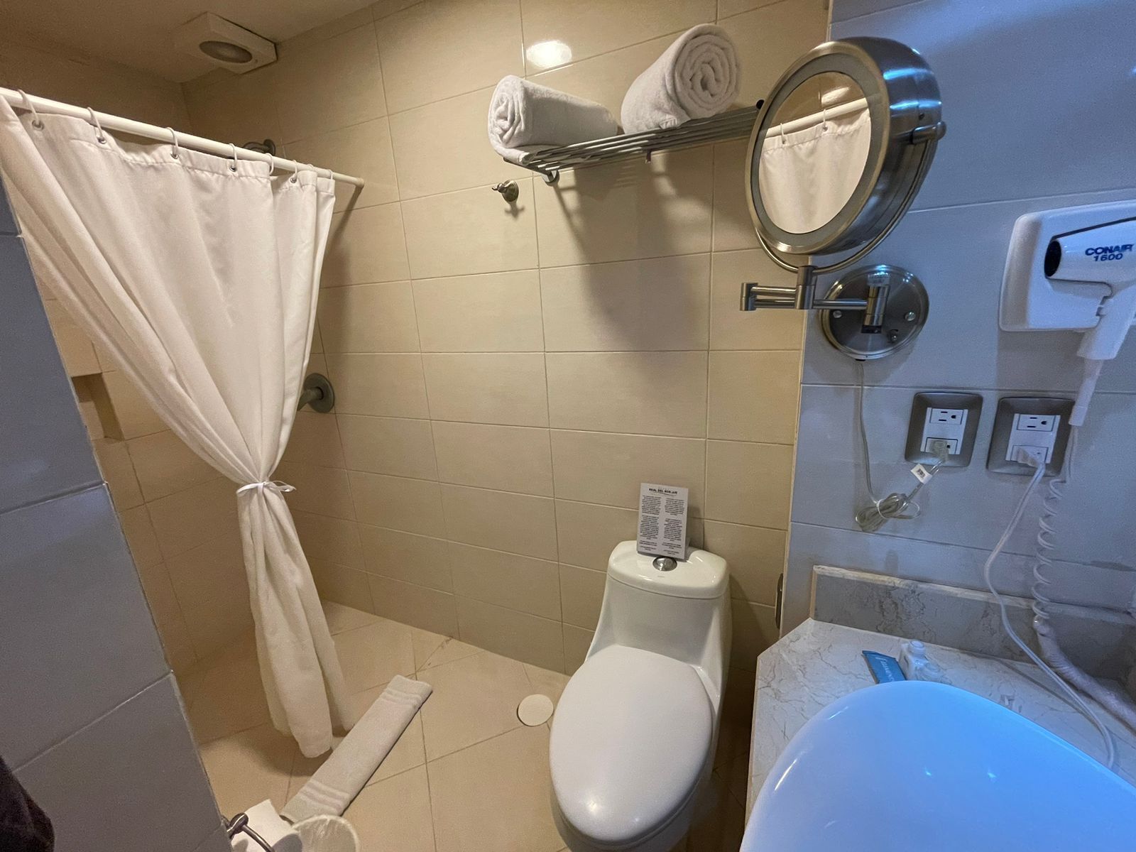 A bathroom with a toilet, a sink, a towel rack with towels, a shower curtain, and a mirror.