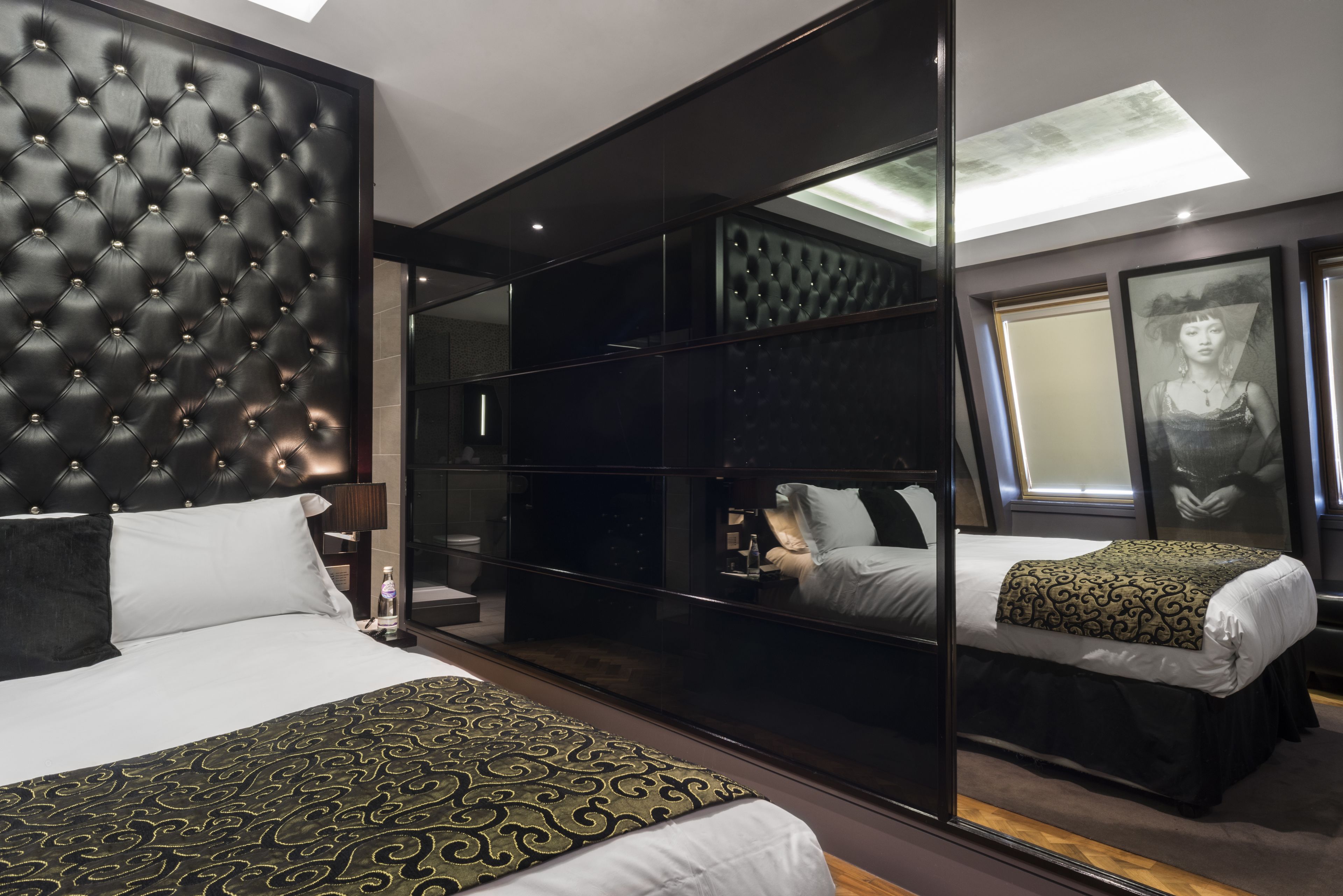 A modern hotel room with a large bed, a mirrored wardrobe, and a skylight.