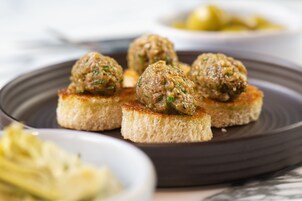 A plate with meatballs on toast, accompanied by a side of pickles.