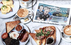 A breakfast spread with toast, beans, eggs, and bacon, along with a newspaper and coffee. - Le Monde Hotel (Edinburgh)