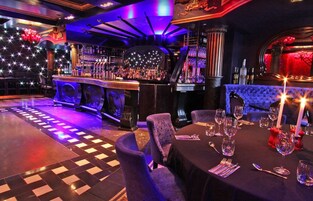 A bar area with a bar counter, shelves with bottles, and a seating area with tables and chairs.