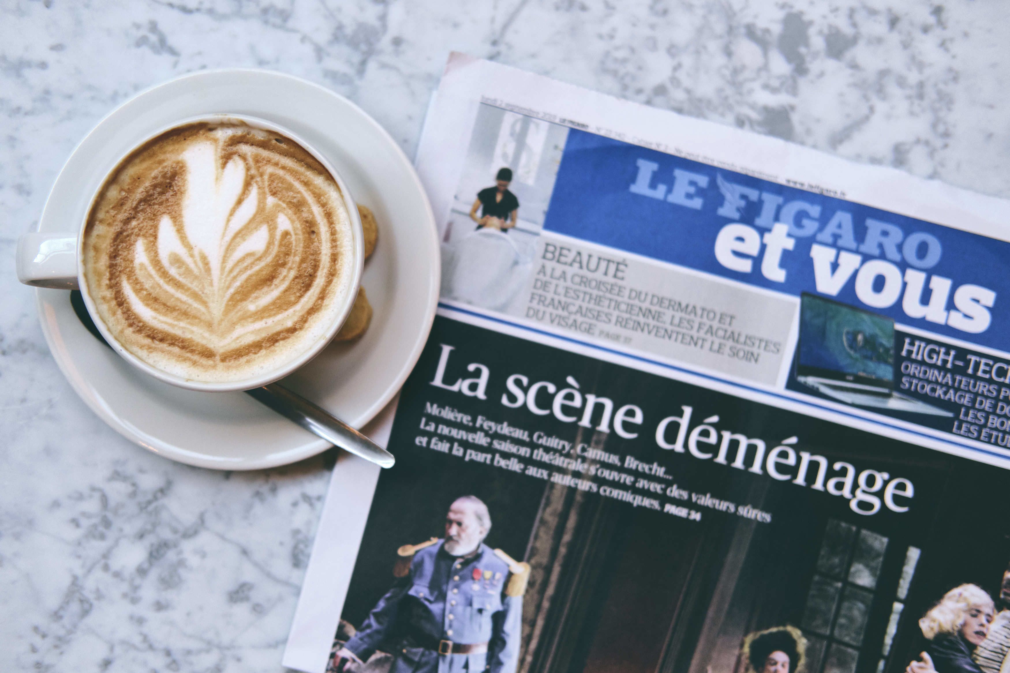 A newspaper with a headline and a cup of coffee with latte art on a marble surface.
