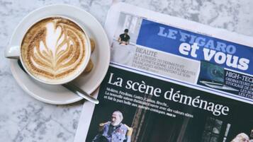 A newspaper with a headline and a cup of coffee with latte art on a marble surface.