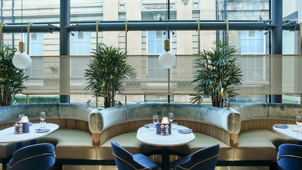 Un restaurante moderno con mesas redondas, sillas azules y una zona de estar curvada.