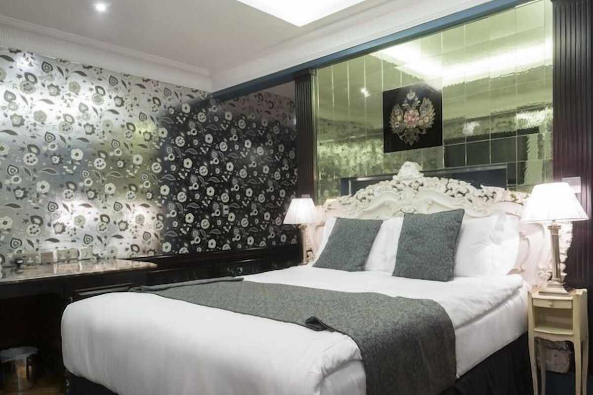A modern bedroom with a large bed, a skylight, a decorative mirror, and a nightstand with a lamp.