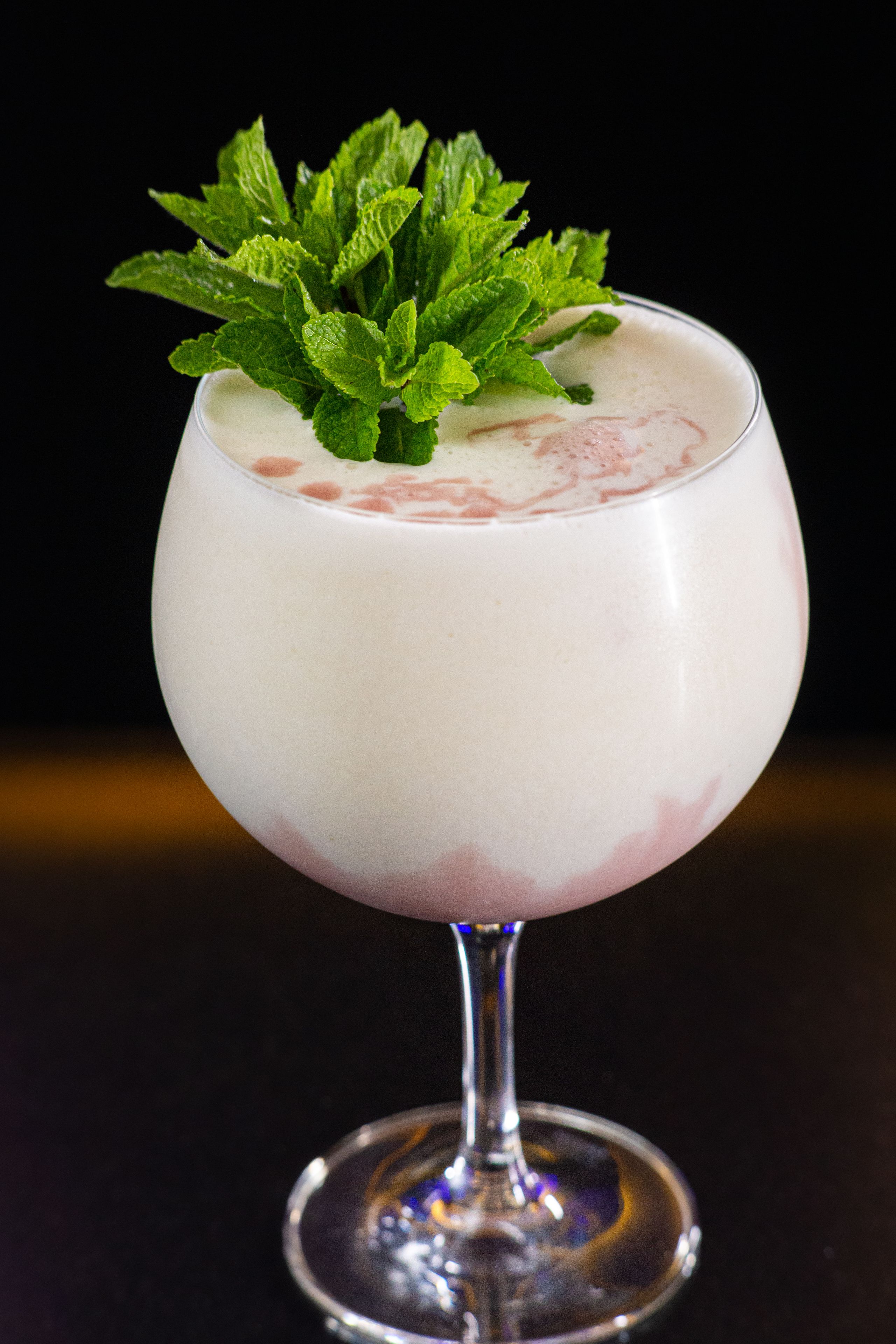 A cocktail in a stemmed glass with a mint garnish.