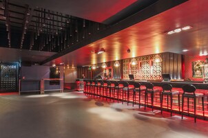 A bar area with a long counter and multiple stools, a staircase, and a decorative wall with geometric patterns.