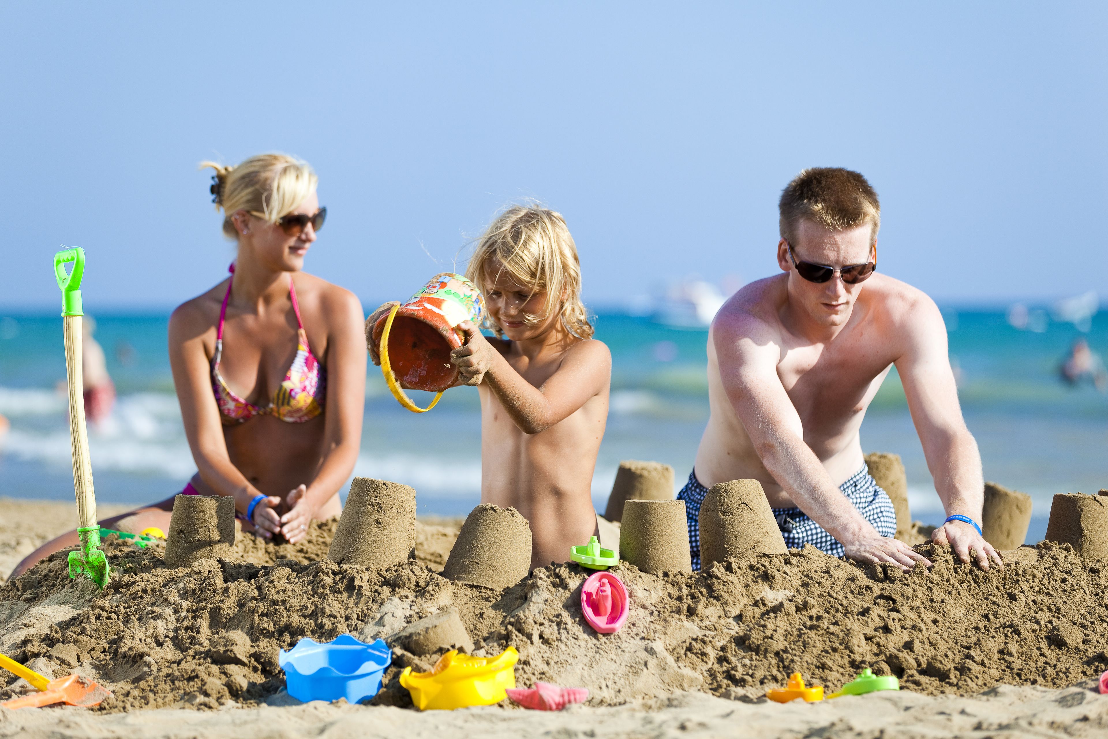 Three people building sandcastles on a beach.