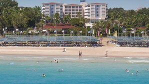 A hotel with multiple floors, a beach in the background, and several flags. - Terrace Beach Resort - All Inclusive (Manavgat)
