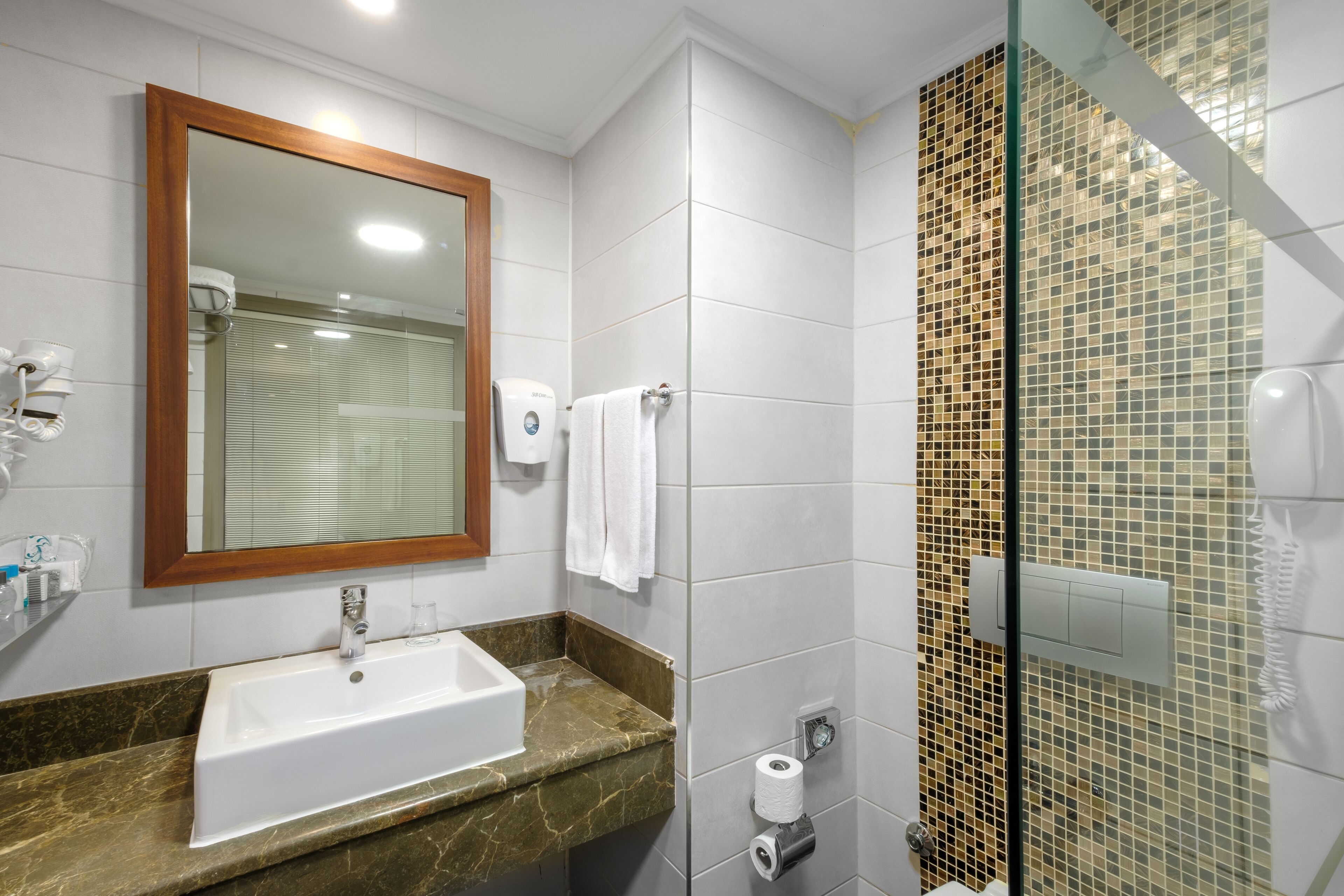 A bathroom with a large mirror, a sink, a glass shower enclosure, and a marble countertop.