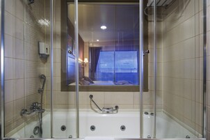Un baño moderno con ducha envuelta en cristal, bañera y espejo que refleja una habitación con ventana.
